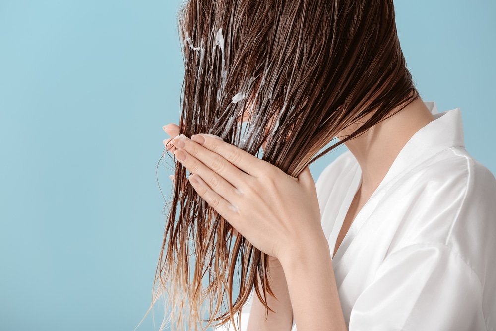 Beautiful young woman applying mousse on her hair after washing