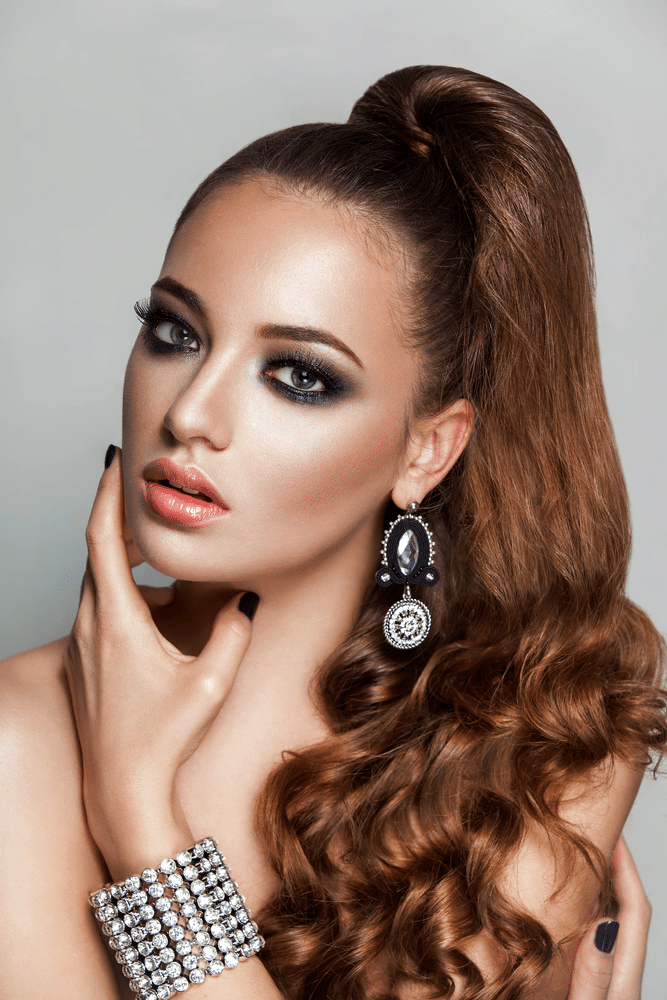 Ponytail hairstyle. Beauty brunette fashion model girl with long healthy curly brown hair and shiny jewelry