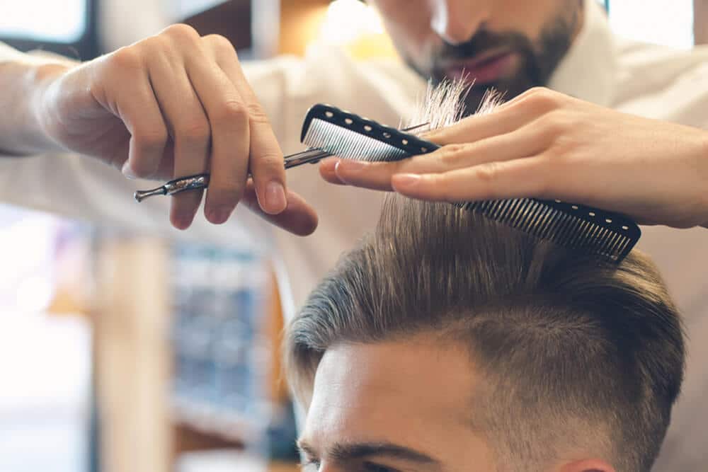 a barber with a scissor and comb trimming the hair of a man