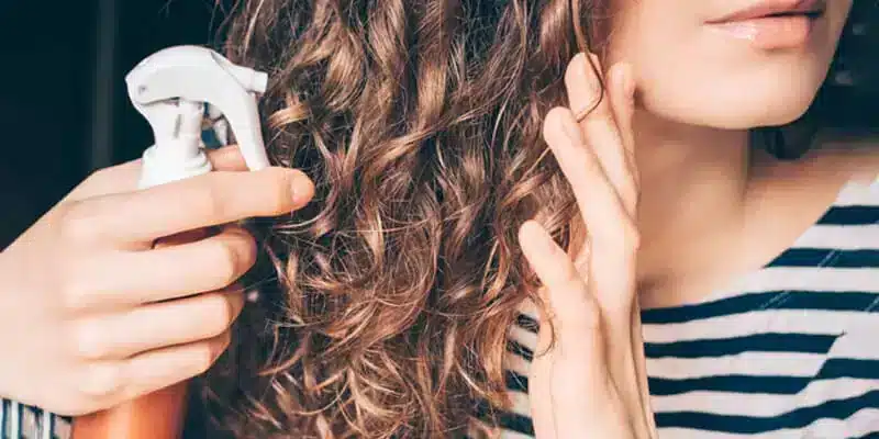 a lady applying protective spray on her hair