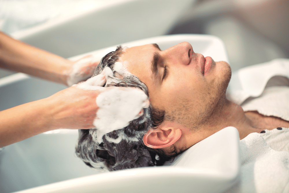 Hairdresser washing hair of handsome client