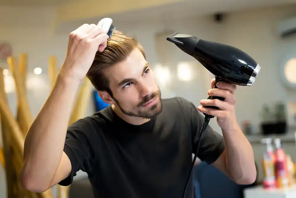 a man blowdrying his hair with a dryer in hand