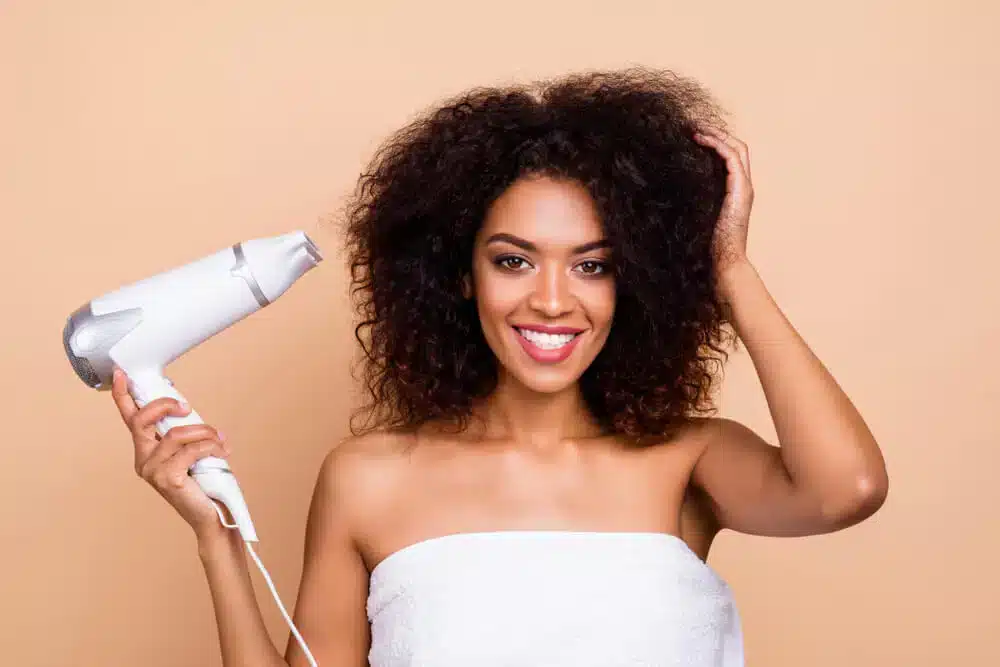 a woman holding a blow dryer in her hand to blowdry her curly hair