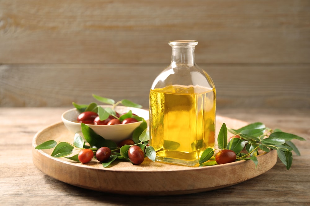 Glass bottle with jojoba oil and seeds on wooden table